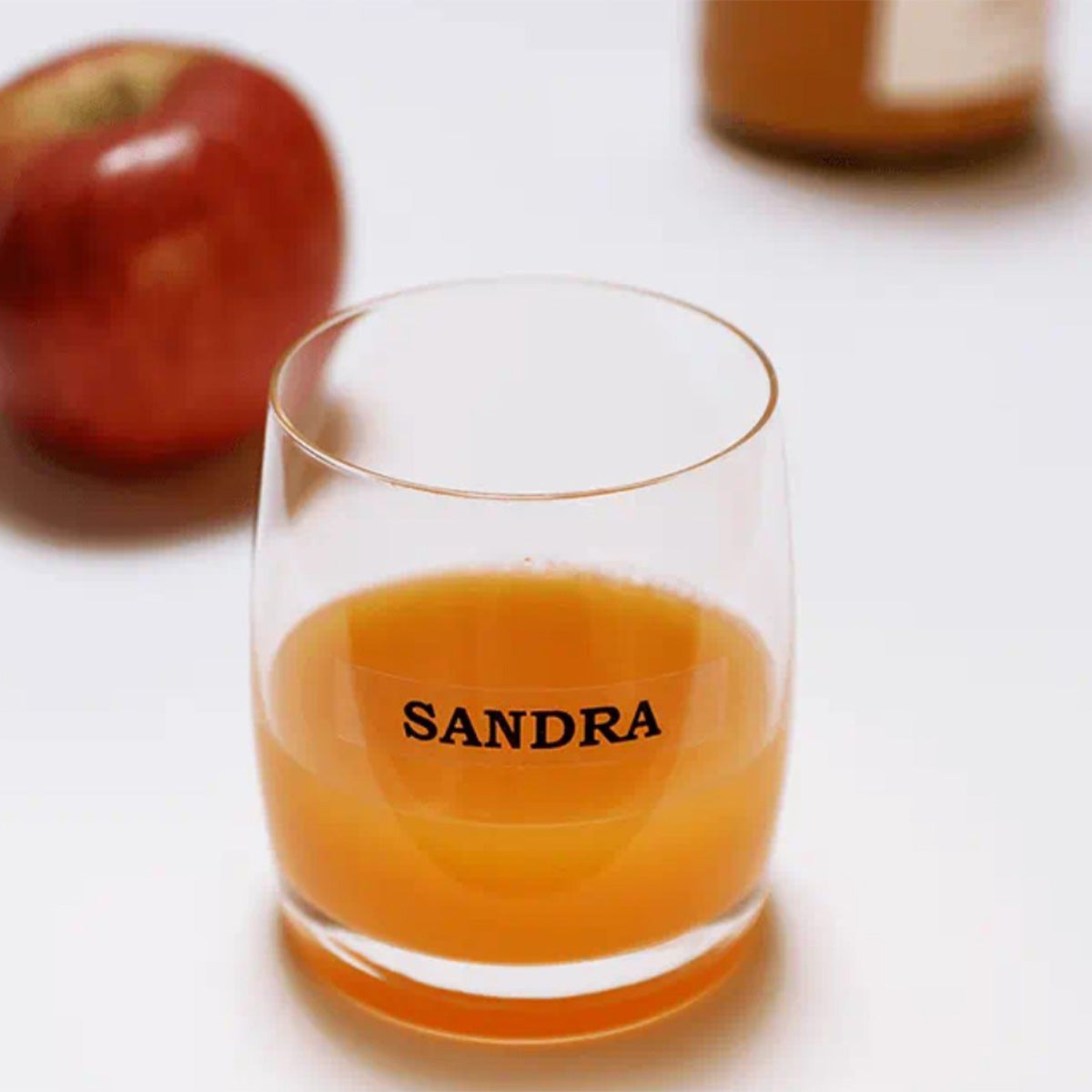Vaso de vidrio con jugo de naranja con una etiqueta transparente letras negras que que permite indicar a quién corresponde o el contenido.