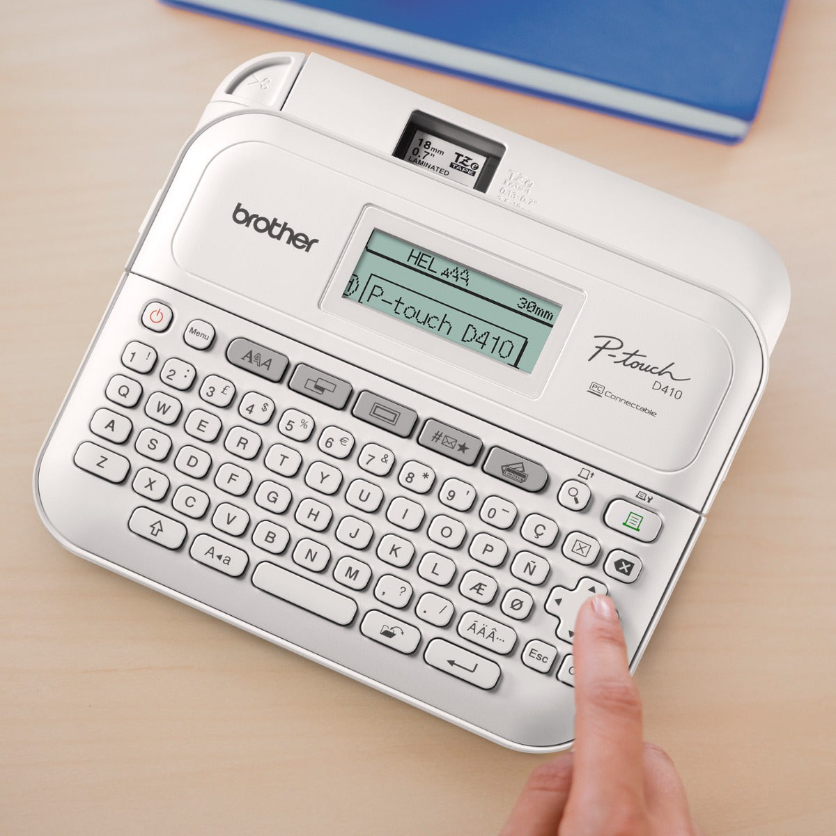 Mano pulsando teclas de una Rotuladora Brother modelo PT-D410 sobre un escritorio de madera.